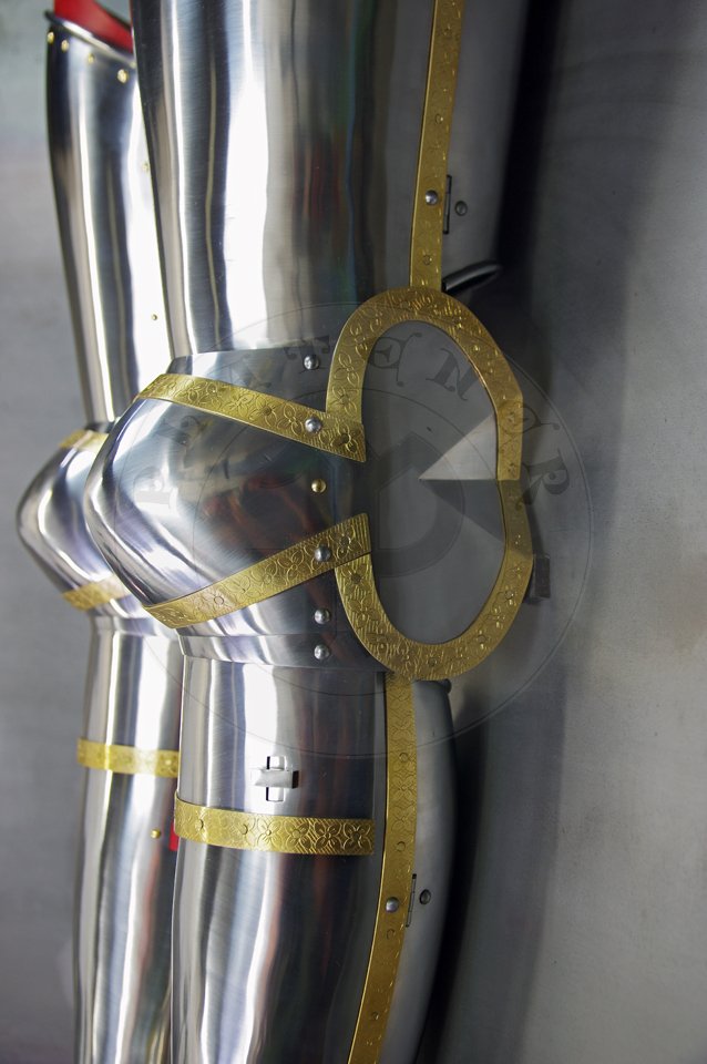English style leg harness with fully closed cuisses, full greaves with characteristic line around outside ankles. Demi-greaves connected with greaves on rotary pin. Made of medium carbon steel of various thickness from 1 mm up to 1,5 mm. Heat hardened and tempered up to 42 HRC. Brass bands decoration motive based on example visible on Henry V tournament helm. Hand made steel buckles in set./Osony ng w stylu angielskim z w peni zamknitymi nabiodrkami, nagolennicami z charakterystyczn lini wok zewntrznej kostki. Demi-greave poczony z nagolennicami poprzez obrotowy pin. Wykonane ze stali redniowglowej rnej gruboci od 1 mm do 1,5 mm. Hartowane i odpuszczane do 42 HRC. Mosine listwy dekoracyjne z motywem wzorowanym na hemie turniejowym Henryka V. W zestawie rcznie robione sprzczki stalowe.